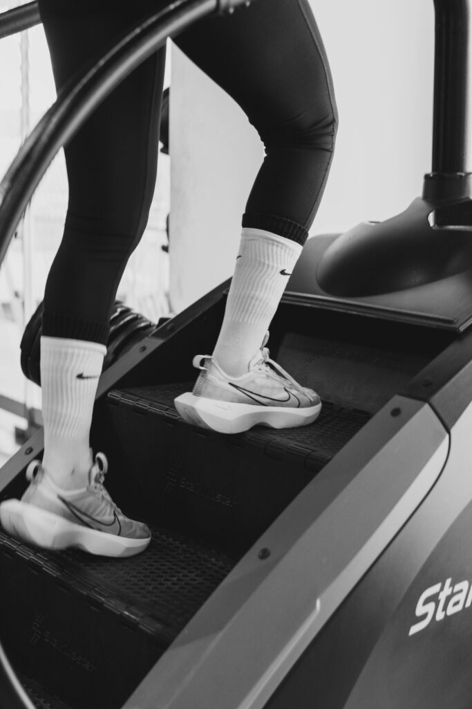 Monochrome shot of person exercising on StairMaster, focusing on legs and sneakers.