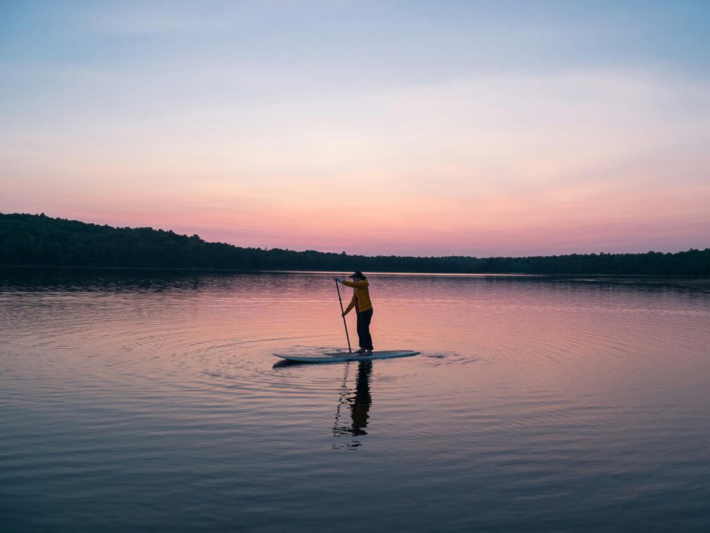 A serene scene of a person paddleboarding on a tranquil lake during sunset, reflecting golden hues.