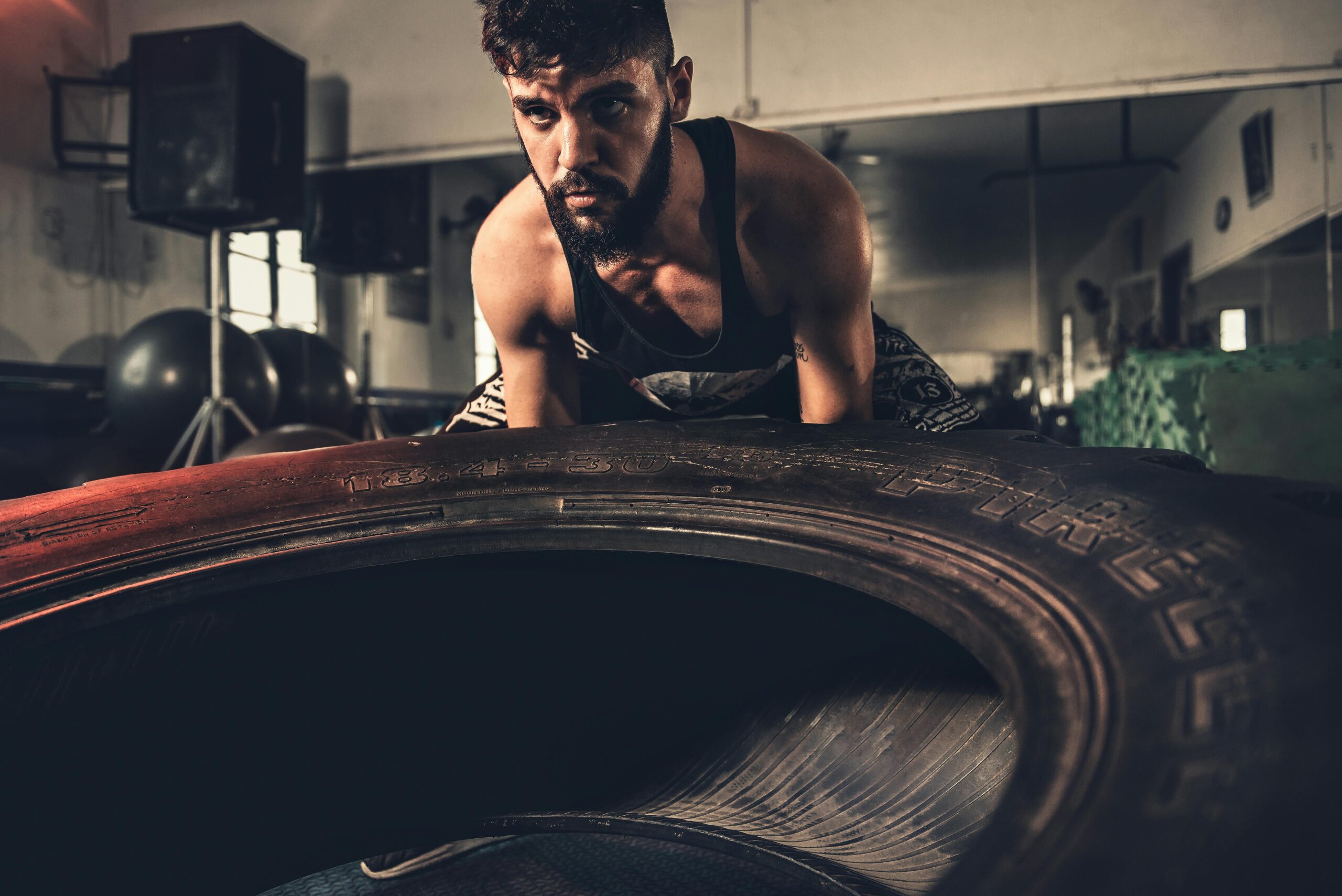 Man focusing intensely while flipping a large tire during a crossfit workout in a gym.