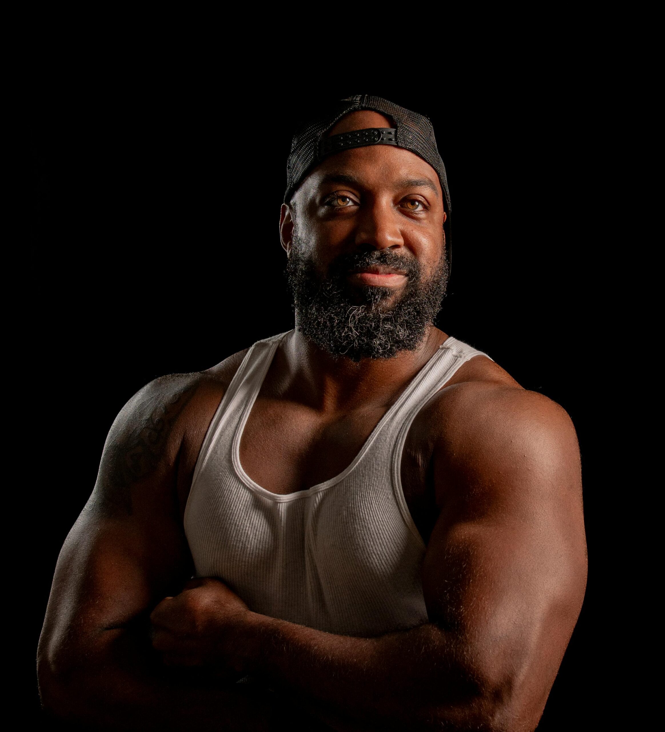 Portrait of a muscular man smiling confidently in a tank top against a dark background.