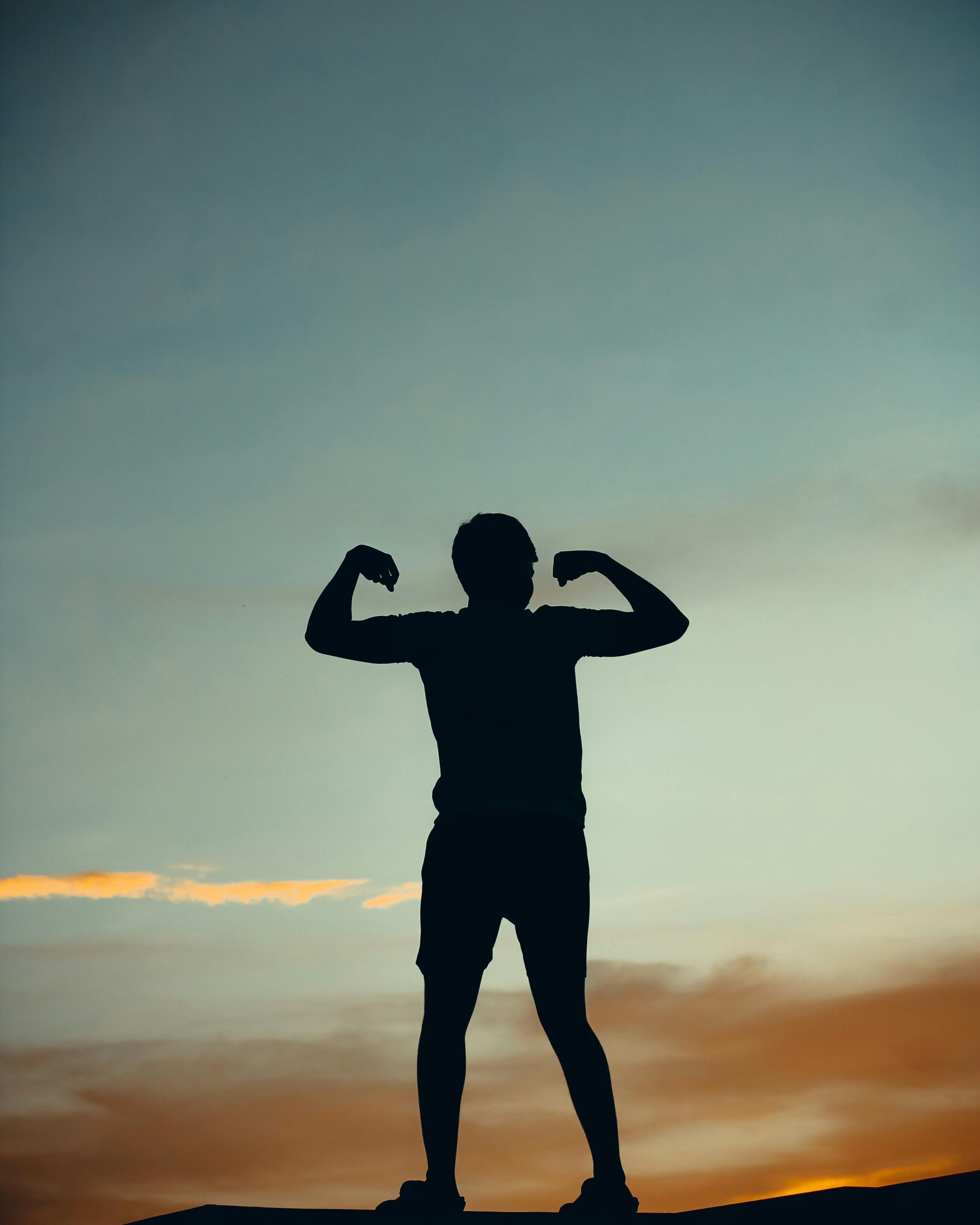 A powerful silhouette of a person flexing muscles against a vibrant sunset sky in India.